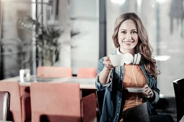 Jovem mulher agradável sorrindo e sugerindo para tentar seu café — Fotografia de Stock