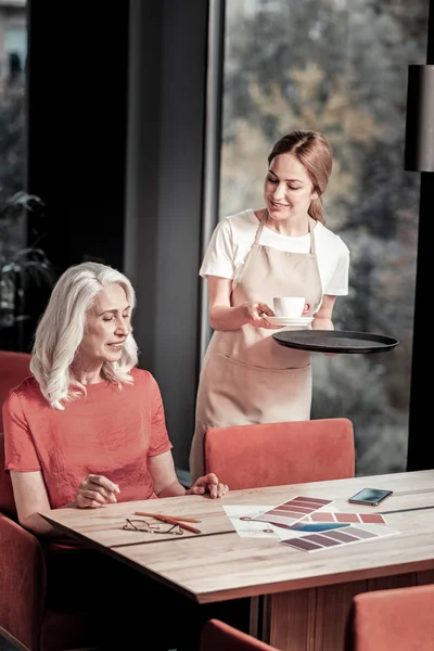 Aangename serveerster een kopje koffie geven een oudere bezoeker — Stockfoto