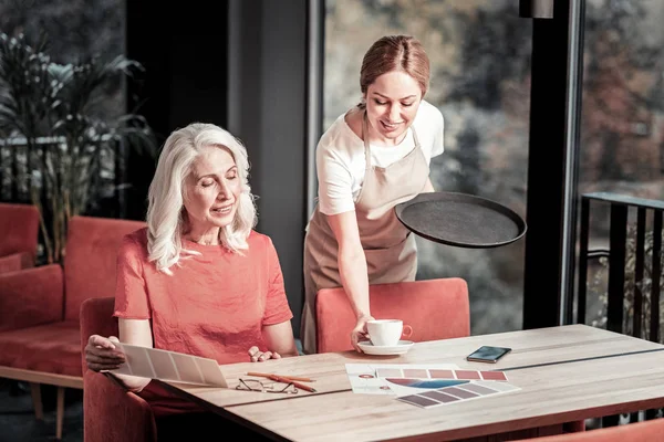 Lächelnde junge Kellnerin reicht Kaffee an einen fröhlichen Besucher — Stockfoto