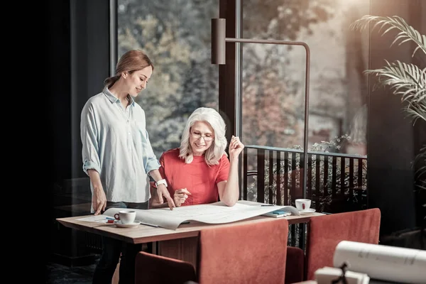 Jonge lachende vrouw toont een gedetailleerde regeling aan haar collega — Stockfoto