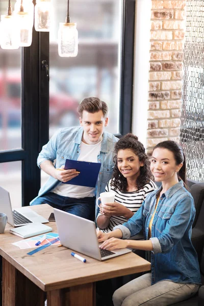 Hombre sonriente prometedor y dos chicas sentadas a la mesa — Foto de Stock