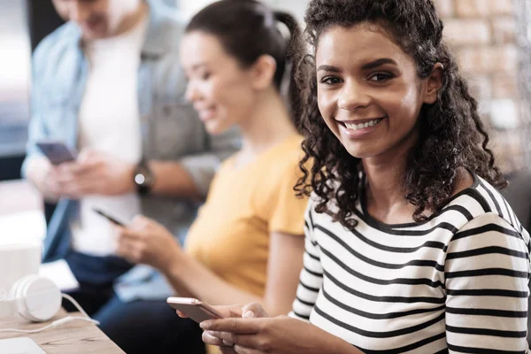 Wachsames lächelndes Mädchen, das sitzt und sein Telefon hält — Stockfoto