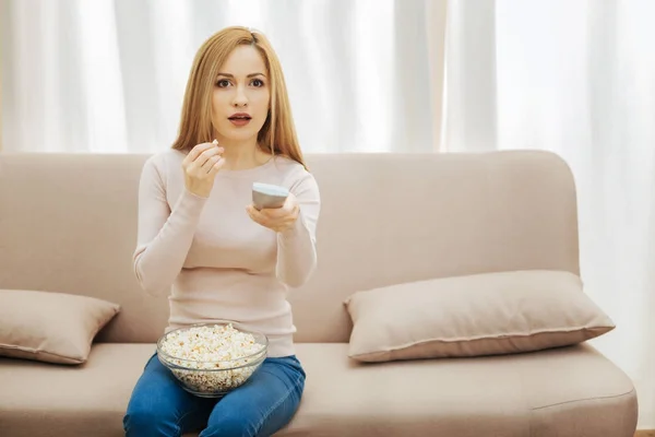 Zdumiony kobieta jedzenie popcorn podczas oglądania telewizji — Zdjęcie stockowe