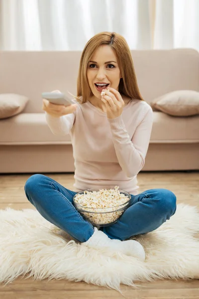 Leende kvinna sitter på mattan med popcorn — Stockfoto