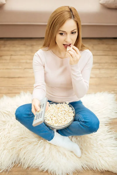 Joyful woman in jeans eating popcorn on the floor — Stock Photo, Image