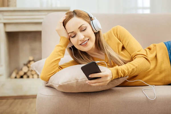 Mujer sonriente relajándose en el sofá y escuchando música —  Fotos de Stock