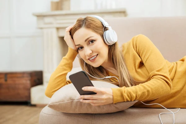 Gladlynt kvinna kopplar av på soffan och lyssnar på musik — Stockfoto
