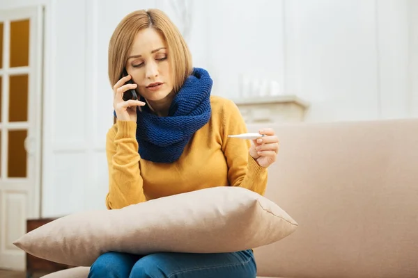 Triste femme tenant un thermomètre et parlant au téléphone — Photo