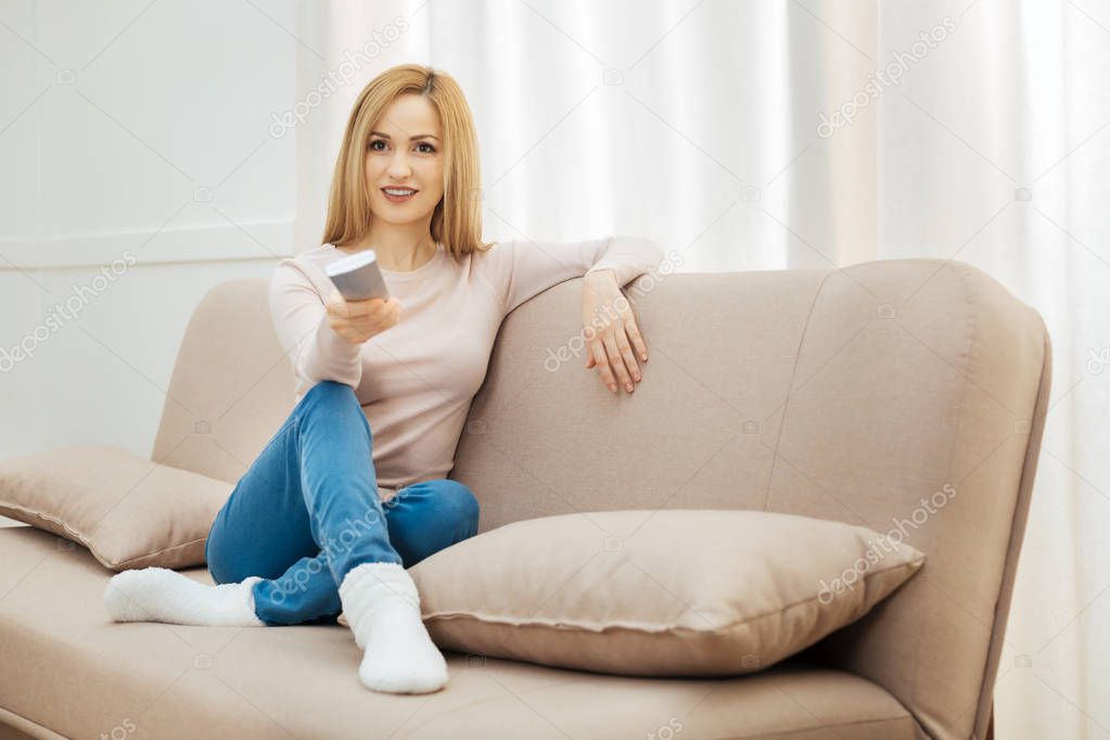 Happy woman sitting on the sofa with remote control