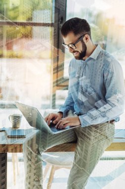 Masada oturan ve dizüstü bilgisayar kullanarak hoş dostça adam.