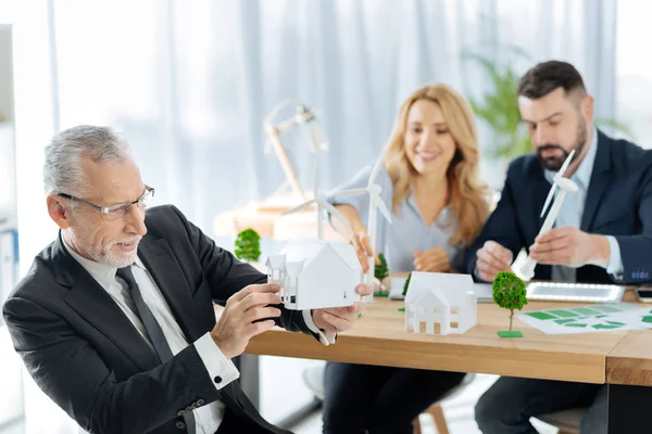 Curious engineer holding a miniature house while his colleagues sitting behind — Stock Photo, Image
