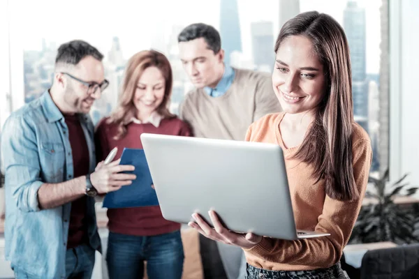 Agradable mujer alegre sosteniendo el portátil y trabajando con él . — Foto de Stock