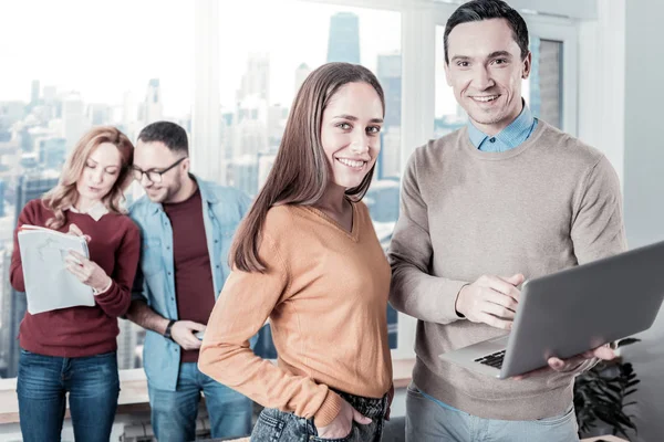 Empleados confiados y alegres trabajando con el portátil y mirando directamente . — Foto de Stock