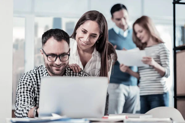 Zufriedener unerschütterlicher Mann, der neben Kollege sitzt und den Laptop benutzt. — Stockfoto