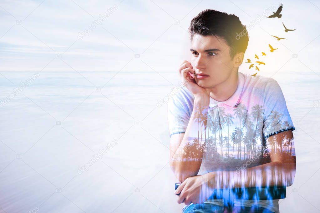 Pleasant handsome thoughtful man holding his chin and imagining palm trees