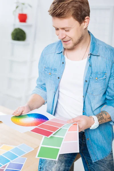 Designer sorridente sentado em seu escritório e olhando para paletas de cores diferentes — Fotografia de Stock