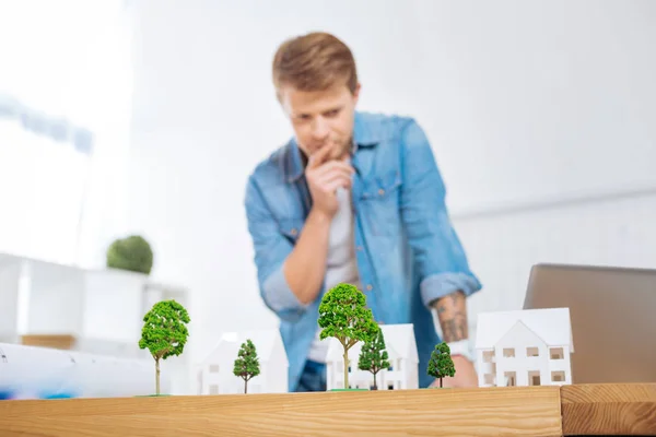 Nachdenklicher Ingenieur runzelt die Stirn und betrachtet die Modelle von Bäumen — Stockfoto