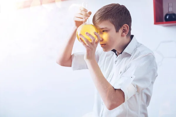 Neugieriger Junge blickt durch Rundbodenflasche im Schullabor — Stockfoto