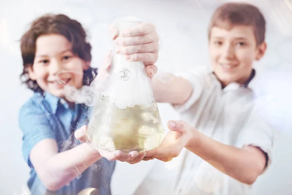 Little happy scientists showing vacuum flask for camera — Stock Photo, Image