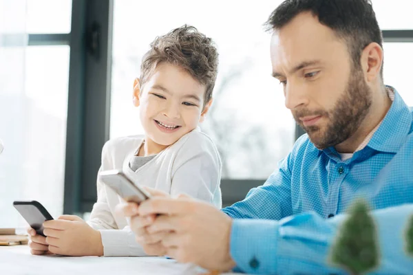 Lively boy peeking at his fathers phone and laughing