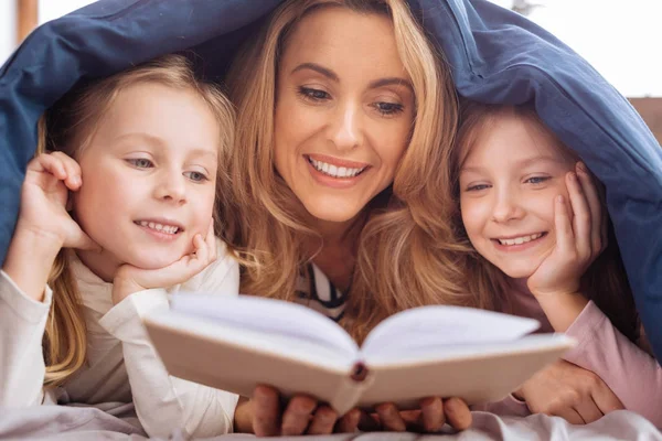Веселая мама читает книгу для своих дочерей — стоковое фото