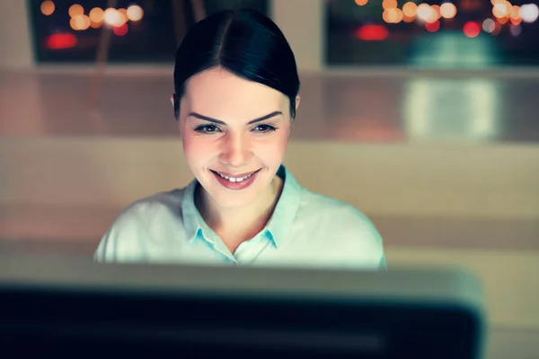 Весела жінка працює на офісному комп'ютері і посміхається — стокове фото