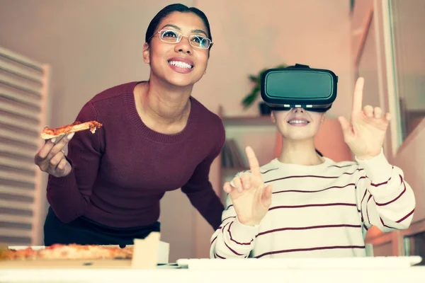 Glada kvinna äter pizza medan hennes kollega använder Vr headset — Stockfoto