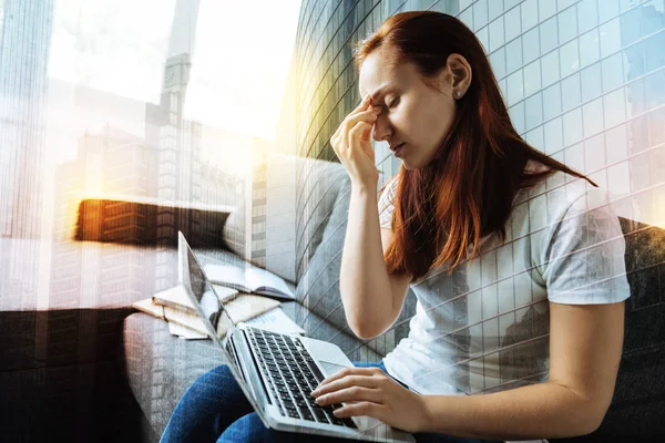 Mulher exausta fechando os olhos enquanto sentada com um laptop — Fotografia de Stock