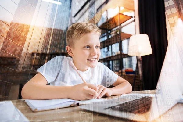 Smart Boy lächelt, während er seine Hausaufgaben macht — Stockfoto