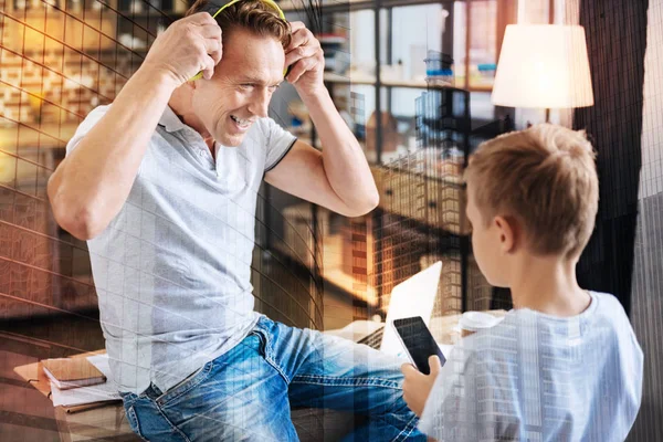 Hombre feliz usando auriculares mientras su hijo sostiene un teléfono inteligente — Foto de Stock