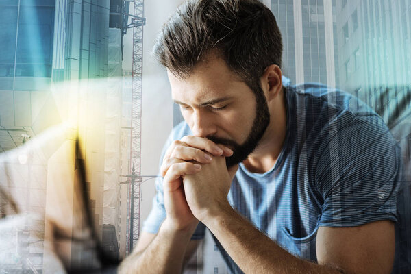 Serious concentrated man closing eyes and holding hands near mouth.