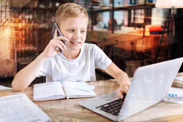 Băiatul zâmbitor vorbind la telefon în timp ce se uita la laptop — Fotografie, imagine de stoc