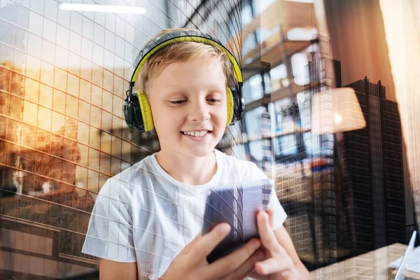 Niño alegre mirando el teléfono inteligente mientras escucha música en los auriculares — Foto de Stock