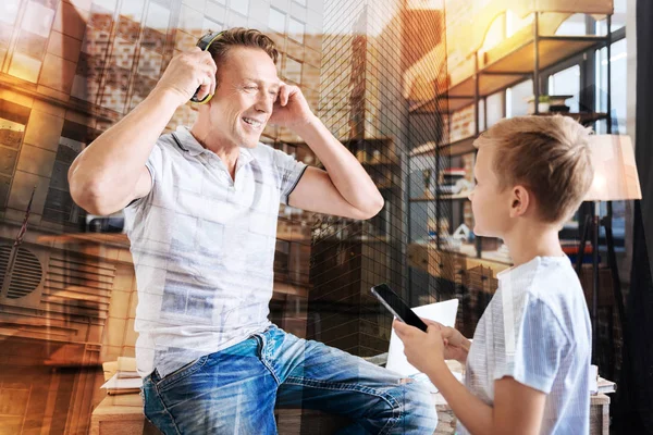 Váltás a zene, miközben mosolyogva apja fejhallgató viselése kíváncsi fiú — Stock Fotó