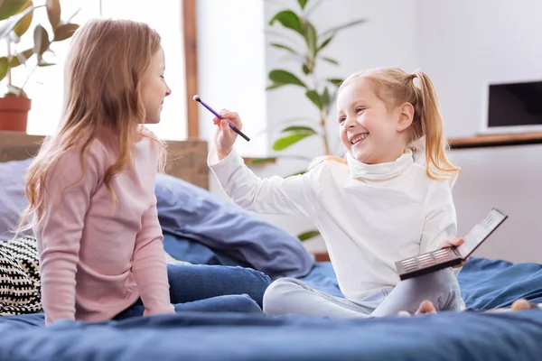 Exuberante hermana menor poniendo maquillaje en su cara hermanas mayores — Foto de Stock