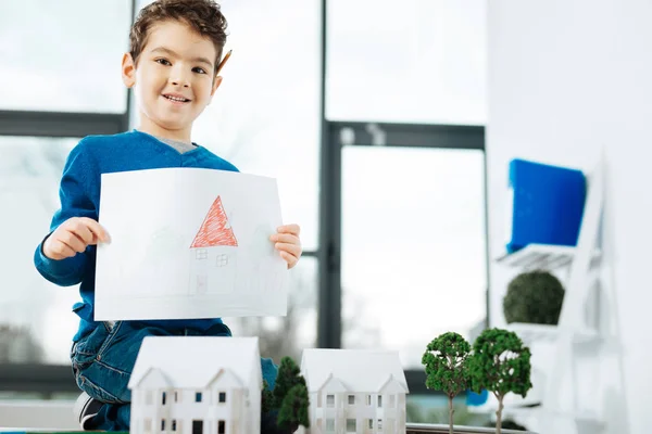 Menino sentado na mesa e posando com uma foto — Fotografia de Stock