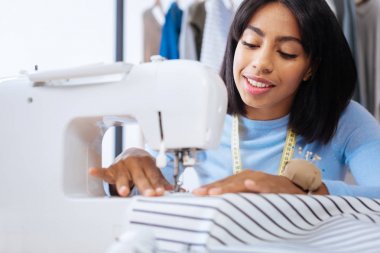 Özenli bir modern uygun dikiş makinesi kullanırken gülümseyerek terzi