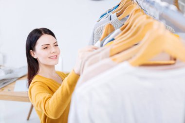 Yeni elbiselere bakarken gülümseyen pozitif genç kadın