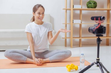 Bir yoga mat üzerinde oturan ve onun izleyicilere konuşurken gülümseyen blogger