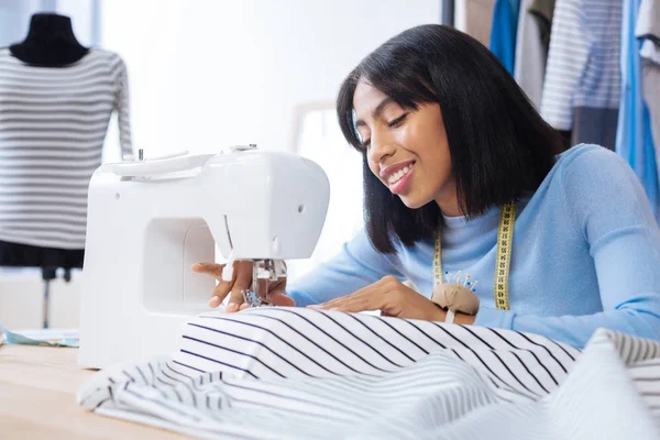 Mujer cuidadosa sonriendo y trabajando en una máquina de coser — Foto de Stock