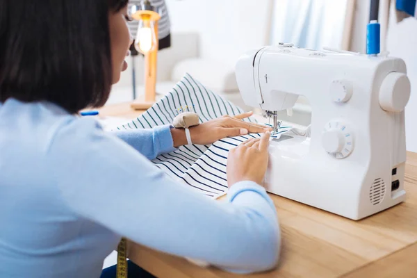 Внимательный портной пришивает полосатый кусок ткани к швейной машинке — стоковое фото