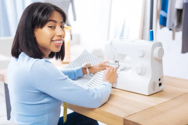 Alegre sastre sentado con sus manos en una máquina de coser y sonriendo — Foto de Stock