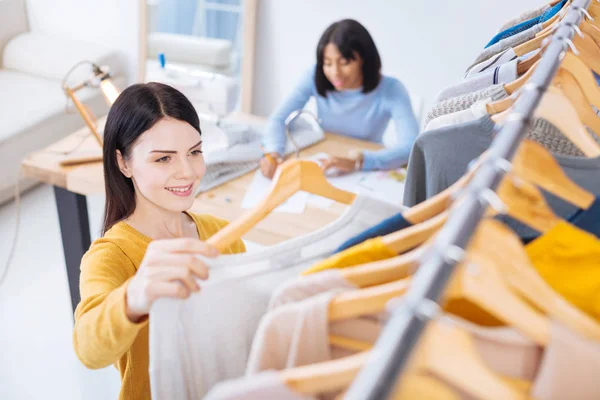Tevreden werknemer kijken naar de kleren gemaakt in haar atelier en glimlachen — Stockfoto