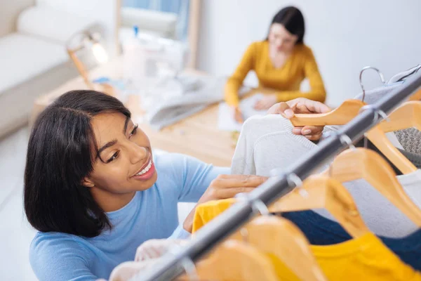 Sonriente mujer alegre haciendo orden mientras que pone perchas en un carril —  Fotos de Stock