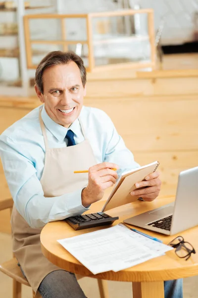 Satisfeito empreendedor gay trabalhando com o laptop e fazendo avisos . — Fotografia de Stock