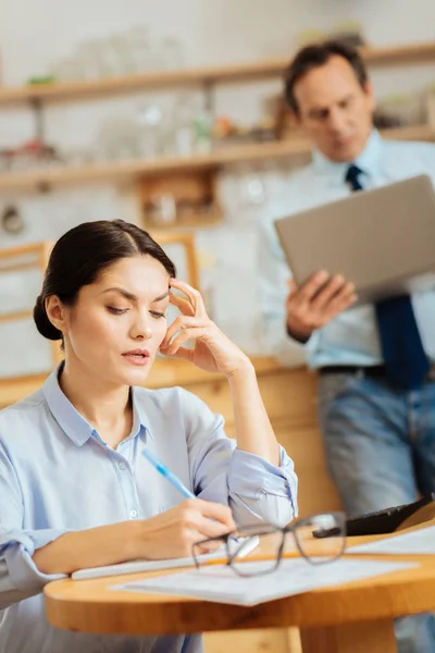 Mujer profunda y reflexiva escribiendo y sosteniendo la mano cerca de la cabeza . — Foto de Stock