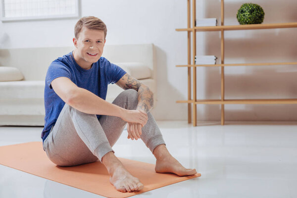 Cheerful online trainer smiling while sitting on the yoga mat