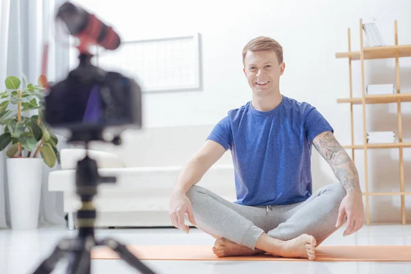 Guapo profesor de yoga sonriendo mientras está sentado en una pose de loto —  Fotos de Stock