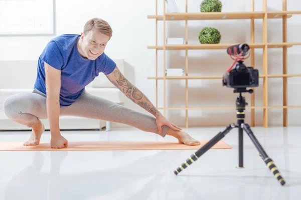 Hombre positivo estirándose en su esterilla de yoga mientras sonríe a la cámara — Foto de Stock