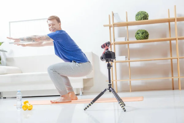 Blogueiro sorridente dobrando os joelhos na frente de uma câmera moderna — Fotografia de Stock